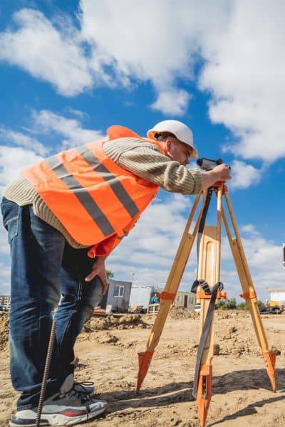 Construction site land surveyor - ALTA SURVEY Tennessee A land surveyor using leveling equipment on a construction site to check elevation and gather data for an elevation survey