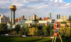 Theodolite on tripod in front of downtown Knoxville, TN skyline during golden hour, highlighting urban land surveying for ALTA survey purposes.