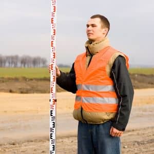Licensed land surveyor measuring ground elevation with a survey rod as part of preparing a flood elevation certificate for property evaluation