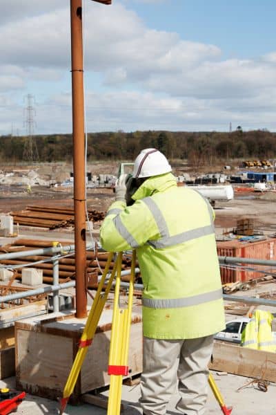 Construction surveyor using equipment to measure site layout and ground elevation before construction begins