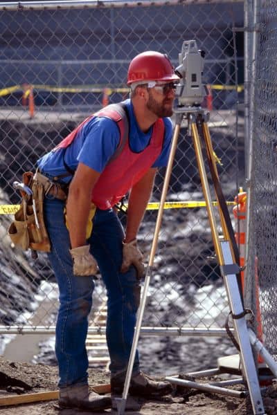 Licensed land surveyor using equipment to perform a lot survey and measure property boundaries