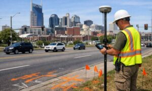 A land surveyor uses GNSS GPS equipment to measure a transportation corridor ahead of planned road, sidewalk, and transit improvements